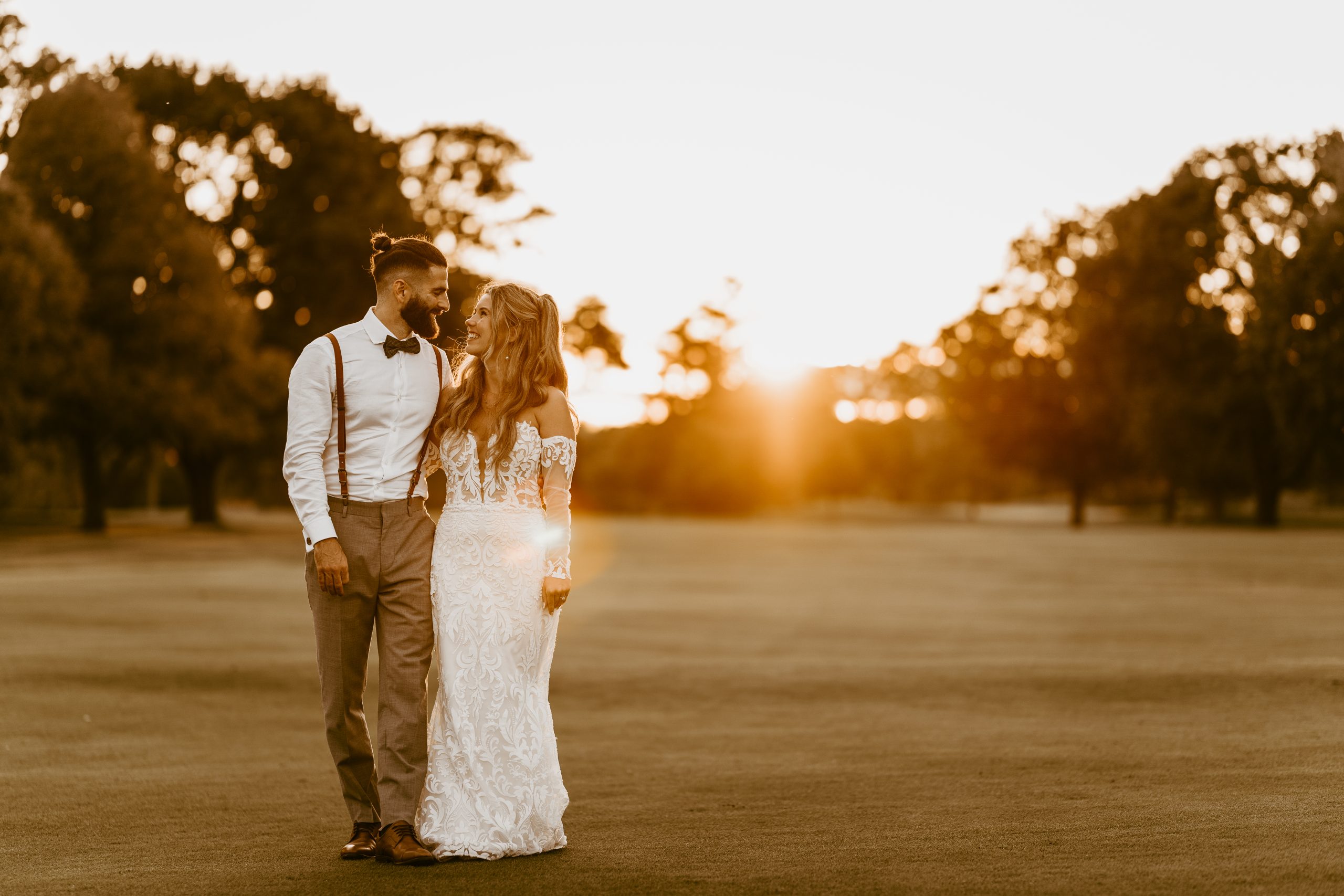 bride and groom walking hand in hand on a golf course during sunset