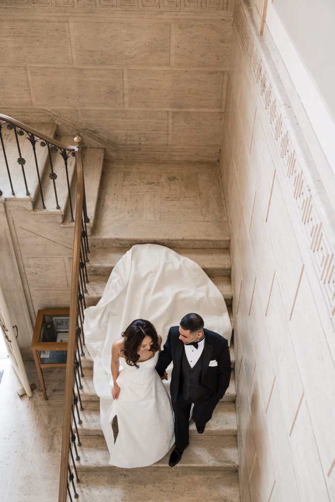 bride and groom walk hand in hand down a set of stairs