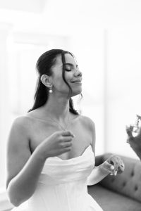 A woman in a strapless dress smiles with her eyes closed, enjoying a moment. Her hair is styled back with loose strands framing her face, and she wears drop earrings. The black and white photo exudes editorial elegance, perfect for wedding inspiration.