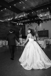 A bride in a white gown and a groom in a dark suit walk hand-in-hand into an elegant, candle-lit Toronto wedding reception hall with wooden walls and string lights overhead, perfect for an editorial-worthy celebration.