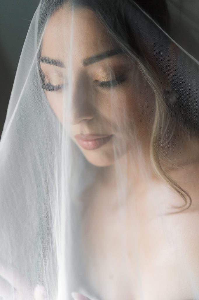 A woman with long eyelashes and softly styled hair is shown with her eyes closed, partially covered by a delicate white veil, captured in a serene and gentle atmosphere by a Toronto wedding photographer.