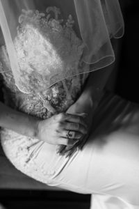 A bride in a lace wedding dress and veil sits with hands folded, showing an engagement ring, beautifully captured in this timeless Toronto wedding photography.