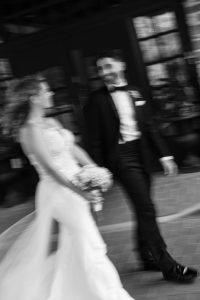 A black and white, motion-blurred photo of a bride holding a bouquet and a groom in a tuxedo walking together, smiling at each other, beautifully captures the candid essence of a Toronto wedding in a documentary style.