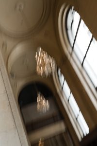 A blurred photo by a talented wedding photographer shows elegant chandeliers hanging from a high arched ceiling with large windows, creating a sense of motion in a grand interior space, perfect for an editorial feature.