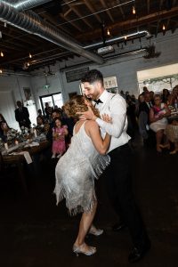 A woman in a sparkly dress and a man in formal wear dance energetically at a wedding reception in Toronto, surrounded by seated and standing guests in a warmly lit venue, capturing the joyful spirit of the celebration in true documentary style.