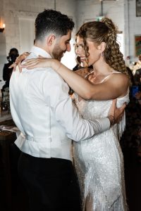 A bride and groom share a joyful first dance at their wedding reception, embracing and smiling at each other in a warmly lit Toronto venue—a perfect moment captured through exquisite photography.