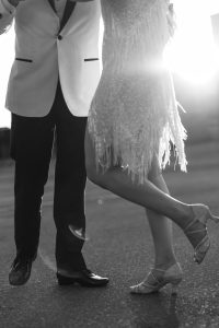 A couple dances in the sunlight; the man wears a suit, and the woman wears a fringed dress and heels. Captured by a talented photographer in Toronto, the image is in black and white.