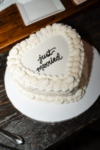 Heart-shaped white cake with decorative icing borders and the words just married written in black icing on top, placed on a white cake board on a dark wooden table—captured in an editorial, documentary style perfect for Toronto weddings.