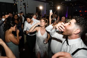 A lively group of people at a wedding party in Toronto, dressed formally, taking shots together on a dance floor with bright lights and energetic expressions, perfectly captured by the photographer.