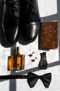 Black dress shoes, floral engraved brown notebook, Stetson cologne, cufflinks, silver watch, black bow tie, and a ring box arranged neatly—perfect details Wedding Photographers Toronto love to capture.