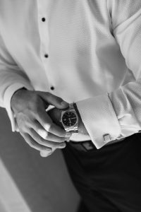 A person in a white dress shirt and dark pants looks at their wristwatch, adjusting the cuff with one hand. Captured in black and white, this image reflects the artistry of Wedding Photographers Toronto.