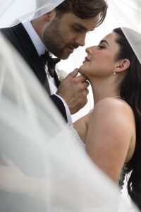 A bride and groom stand closely under a veil, gazing into each other’s eyes lovingly. Captured by Wedding Photographers Toronto, their joyful expressions and soft light create a beautifully romantic atmosphere.