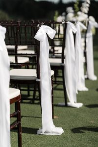 Rows of dark wooden chairs with white cushions and long white ribbons tied in bows are set outdoors on green grass, creating a picturesque scene ideal for Wedding Photographers Toronto to capture a special event.