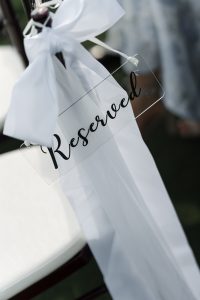 A clear sign with the word Reserved in black script hangs from a chair, decorated with a large white ribbon and sash—perfect inspiration for Wedding Photographers Toronto at any outdoor event.