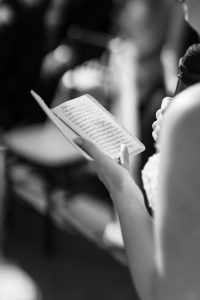 A person holding a notebook and microphone reads handwritten notes during an event. Captured in black and white, this candid moment showcases the artistry of Wedding Photographers Toronto. Only the person’s arm and hand are visible.
