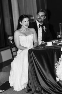A bride in a strapless gown laughs beside her smiling groom in a tuxedo at their wedding reception, both facing the speaker—a candid moment Wedding Photographers Toronto love to capture.