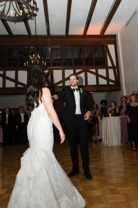 A bride in a white gown and a groom in a tuxedo dance together in a ballroom, surrounded by wedding guests watching and smiling—perfect moments captured by Wedding Photographers Toronto.
