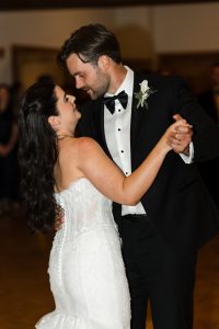 A bride in a white dress and a groom in a black tuxedo share a joyful first dance, beautifully captured by Wedding Photographers Toronto in a warmly lit indoor setting.