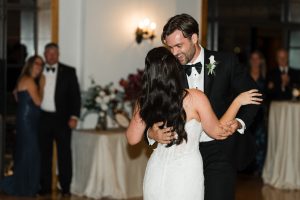 A bride and groom share a joyful first dance at their wedding reception, while guests watch and a couple embraces in the background—captured beautifully by Wedding Photographers Toronto.