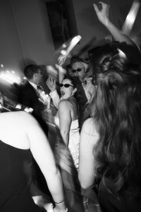 A group of people dance energetically at a party. Some are wearing sunglasses, and blurred lights enhance the lively atmosphere—captured artfully by top Wedding Photographers Toronto in black and white.