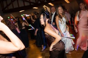 People dancing and smiling at a party, with colorful lights and blurred motion capturing movement and energy—perfect moments for Wedding Photographers Toronto to capture, as a woman in a brown dress stands in the foreground.