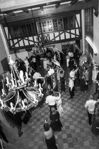 Black and white photo of people dancing in a ballroom with chandeliers and wooden ceiling beams, viewed from above—a timeless moment captured by Wedding Photographers Toronto.